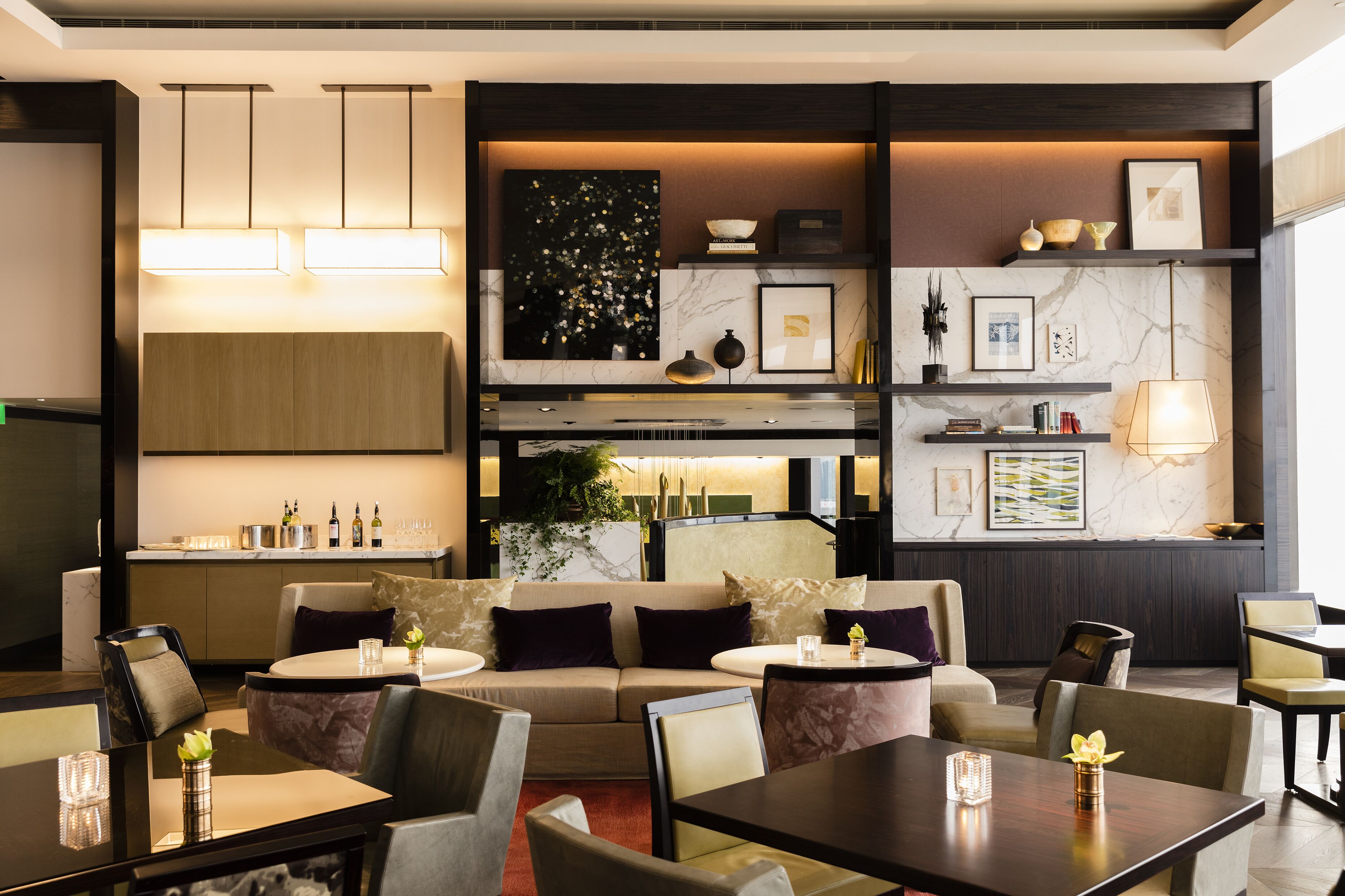 A modern hotel lobby with a sofa, dining tables, and a bar area.