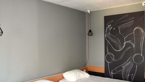 Una habitación de hotel con cama, cabecero, lámpara de pared y un cuadro abstracto grande.