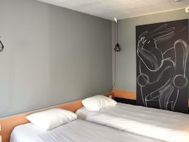 Una habitación de hotel con cama, cabecero, lámpara de pared y un cuadro abstracto grande.