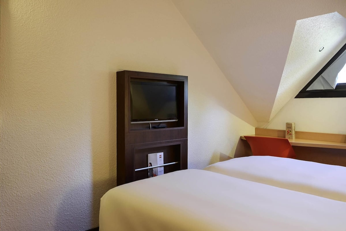 Ein Hotelzimmer mit einem Bett, einem Fernseher, einem Schreibtisch und einem kleinen Fenster.
