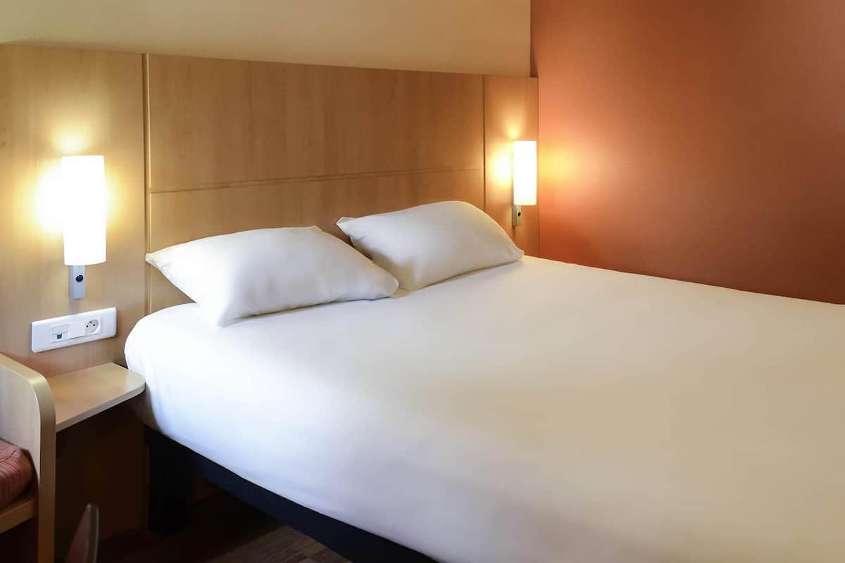 A hotel room with a bed, two bedside lamps, a nightstand, and a power outlet.