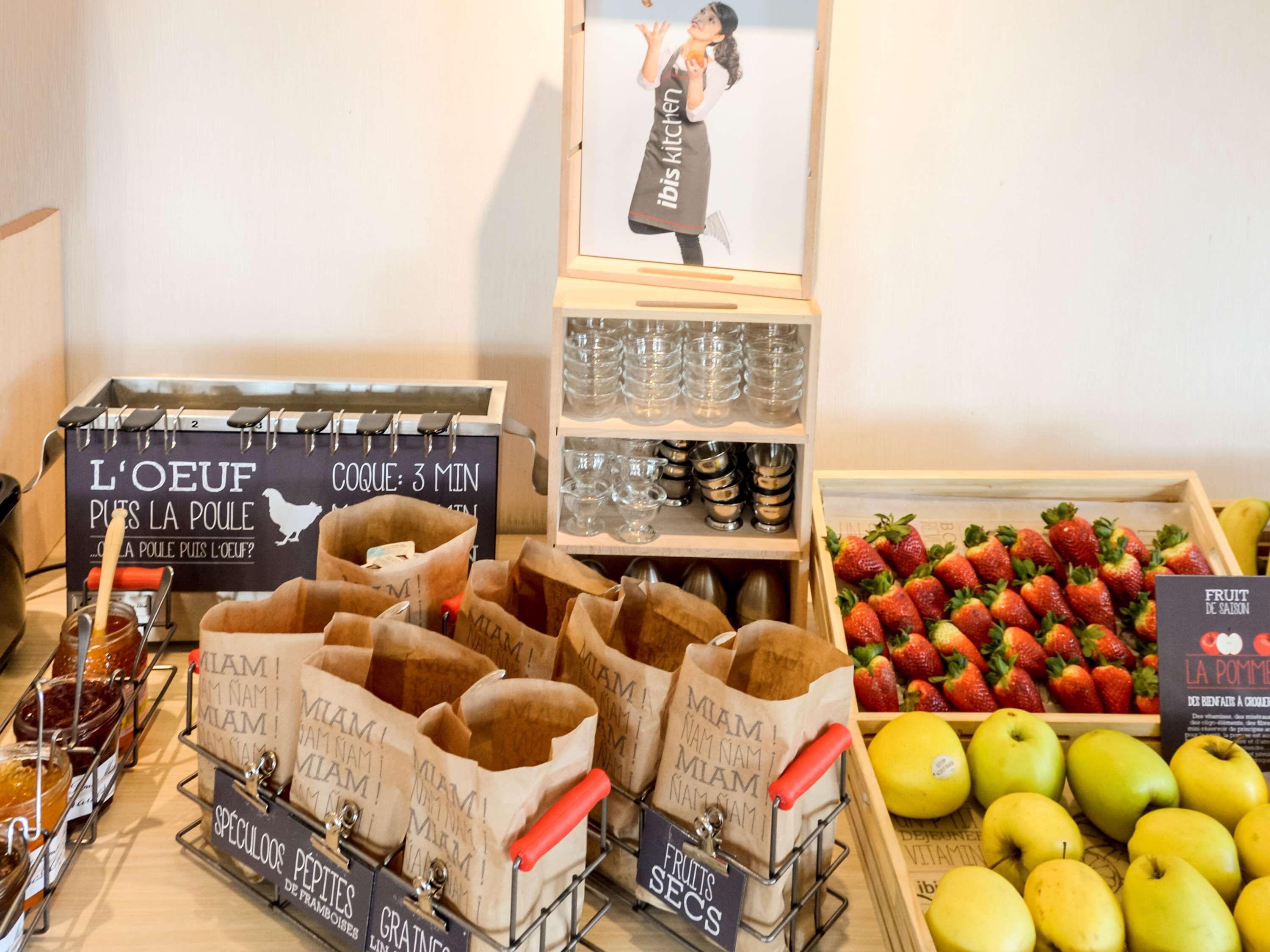 Un bufé de desayuno con alimentos identificados, un letrero con ilustración de un chef y una exhibición de frutas frescas.