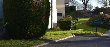 A reception area with a sign for the Récupération Hotel, a building with a white facade, and neatly trimmed hedges.