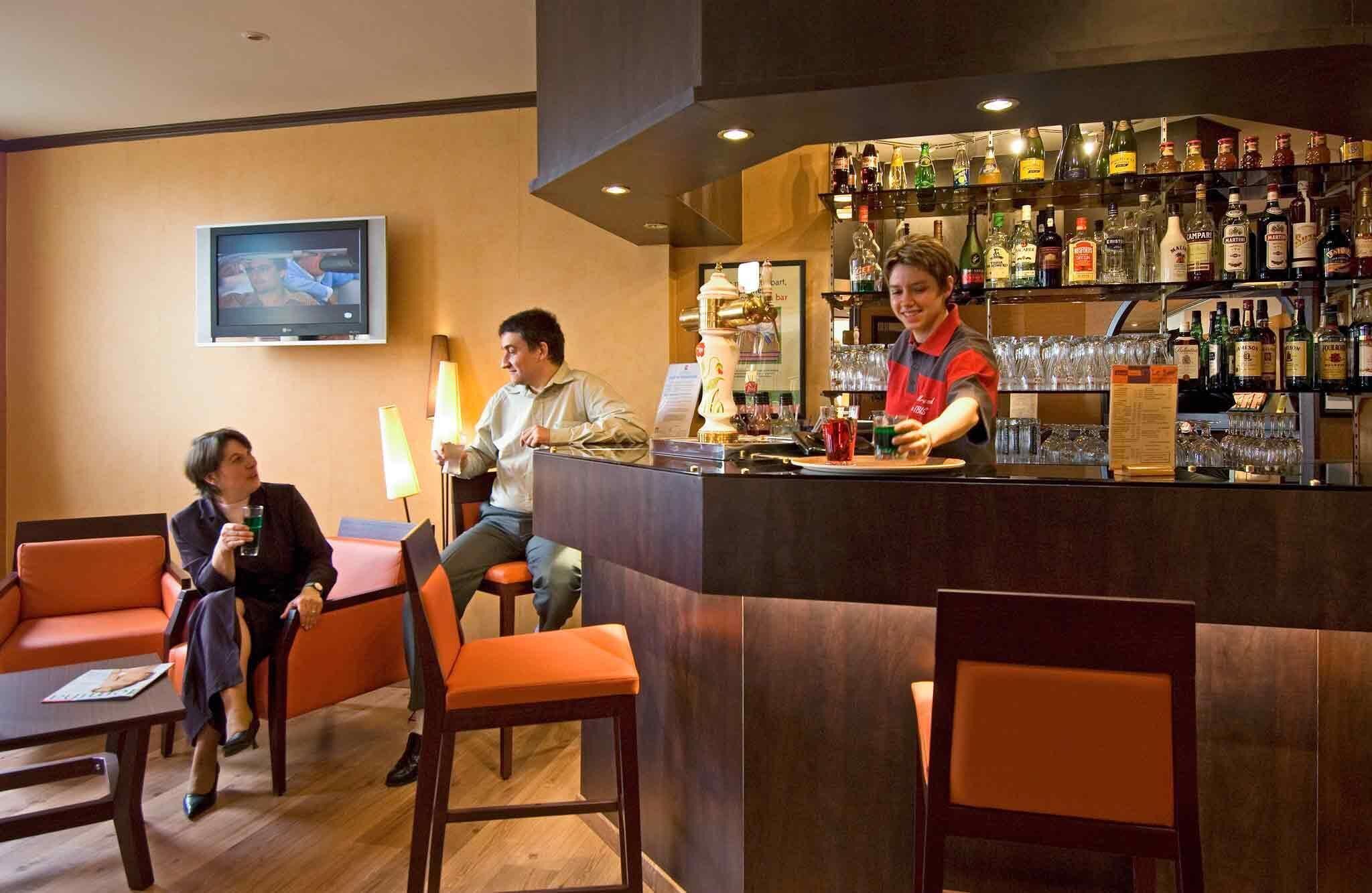 A bar area with seating, a television, and a bartender.