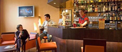 Zona de bar con asientos, un televisor y un barman.