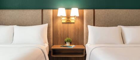 A hotel room with two beds, a wooden headboard, a nightstand with a lamp, and a small plant.