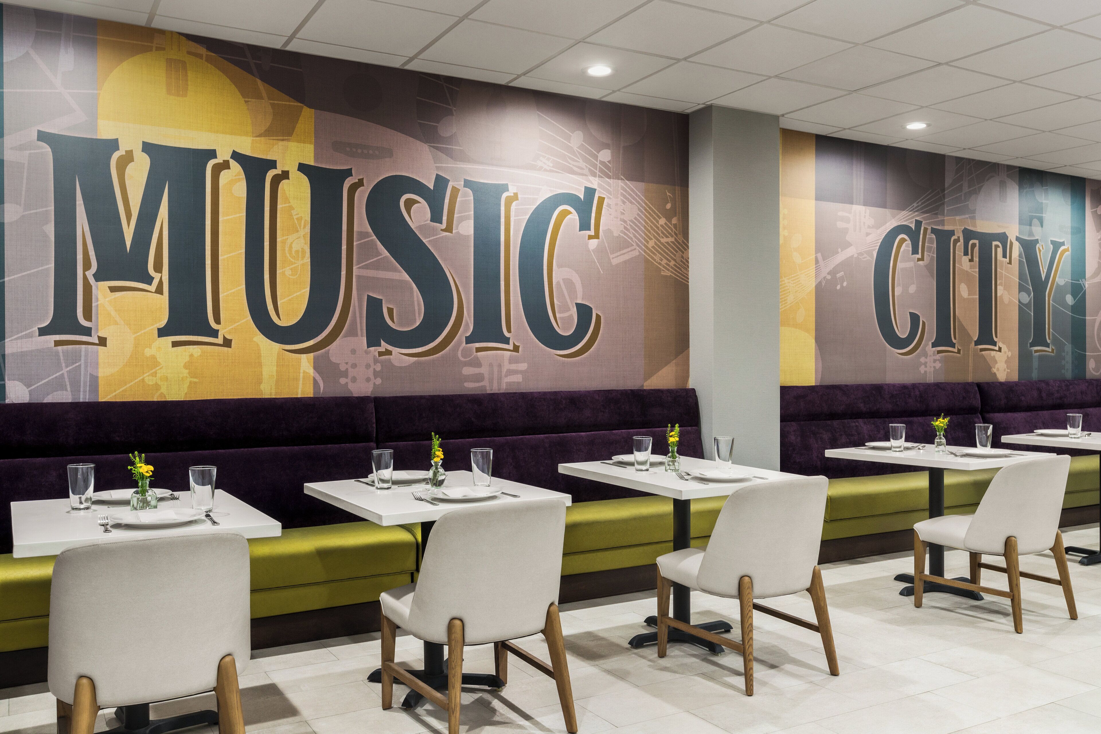 Un restaurante con cabinas y mesas, que presenta un mural grande con la inscripción "MUSIC CITY".