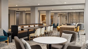 A modern hotel lobby with seating areas, a reception desk, and a visible staircase.