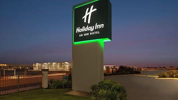 A Holiday Inn sign with a modern design, located in a well-lit area with a view of a cityscape in the background.