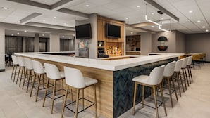 A modern bar area with a long counter, multiple bar stools, and a television screen mounted on the wall.