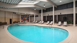 An indoor swimming pool with a skylight ceiling, lounge chairs, and a mural wall.