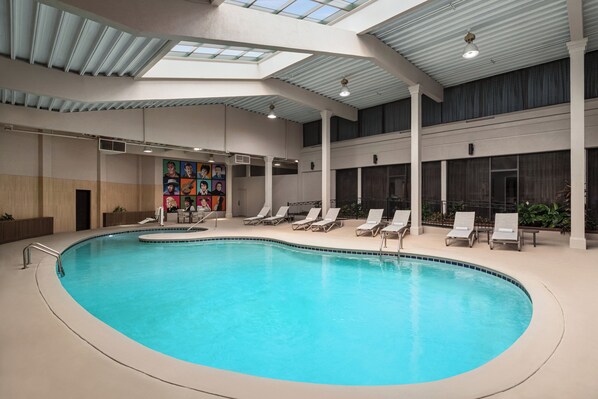 Piscina interior com teto skylight, cadeiras de lounge e um painel decorativo na parede.