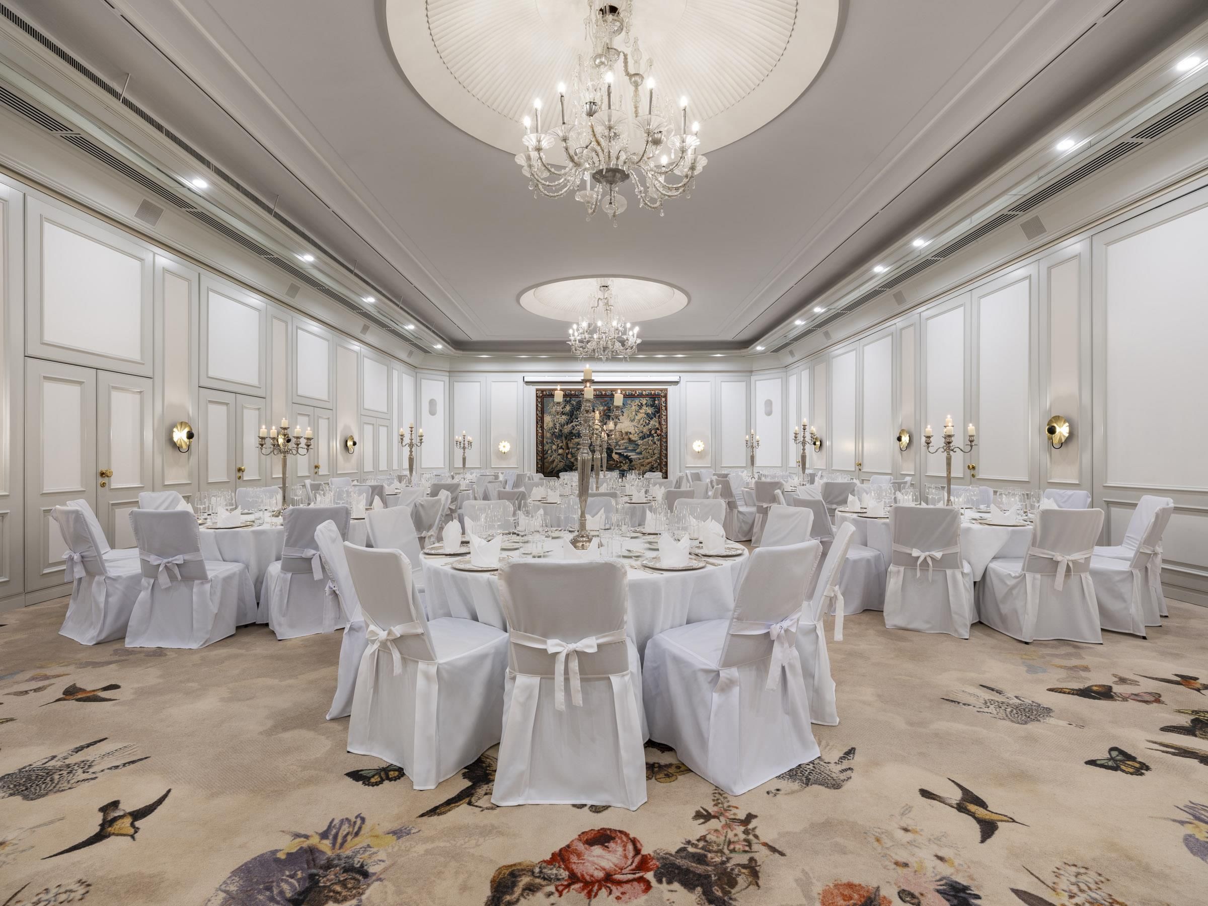 Une salle à manger élégante, avec des tables rondes, des chaises blanches et un lustre.