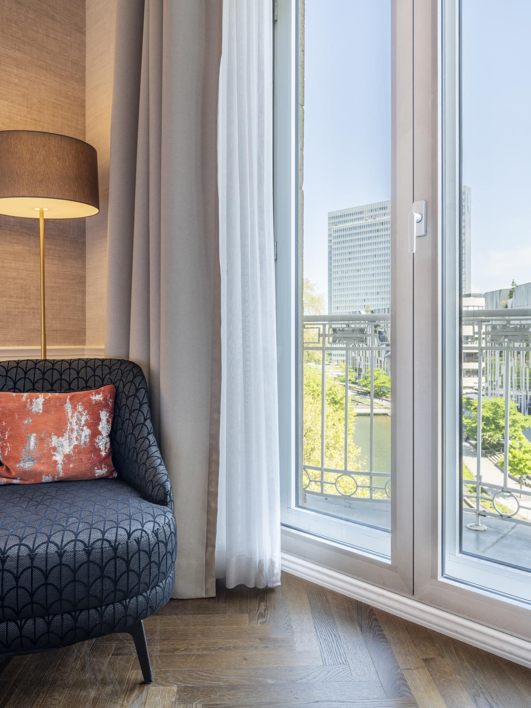 A modern living room with a sofa, a lamp, and a view of a cityscape through large windows.