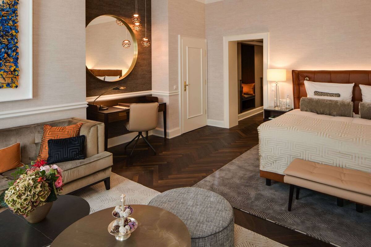 Une chambre d’hôtel comprenant un lit, un bureau, un canapé, une petite table ronde et un grand miroir.