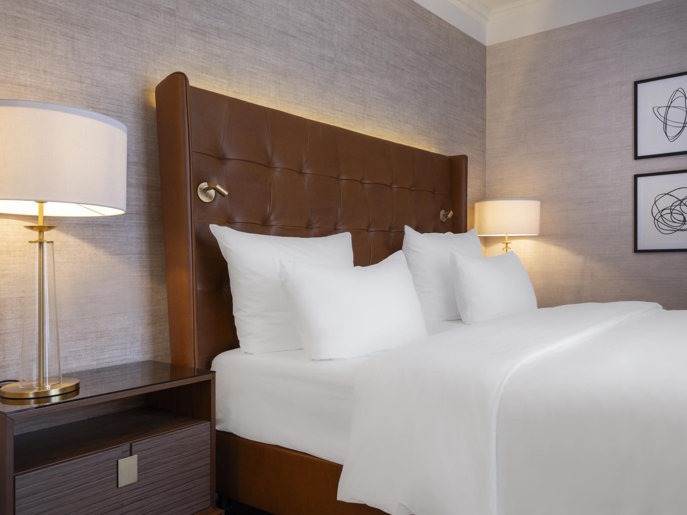 A hotel room with a large bed, two bedside lamps, a nightstand, and a framed abstract artwork on the wall.