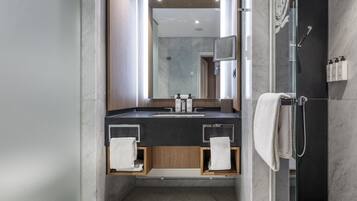 A modern bathroom with a glass-enclosed shower, a marble-tiled floor, and a wooden vanity with a mirror.