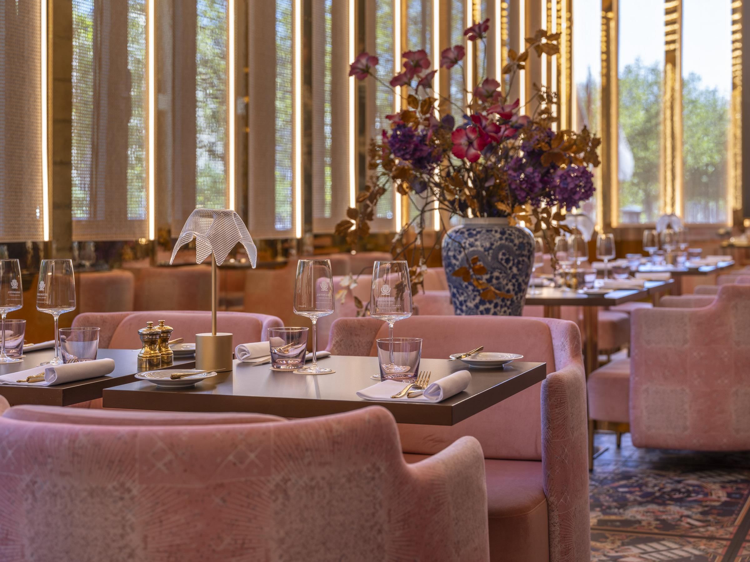 Ein Restaurantinnenraum mit gedeckten Tischen, einer Blumenvase und einem gemusterten Teppich.