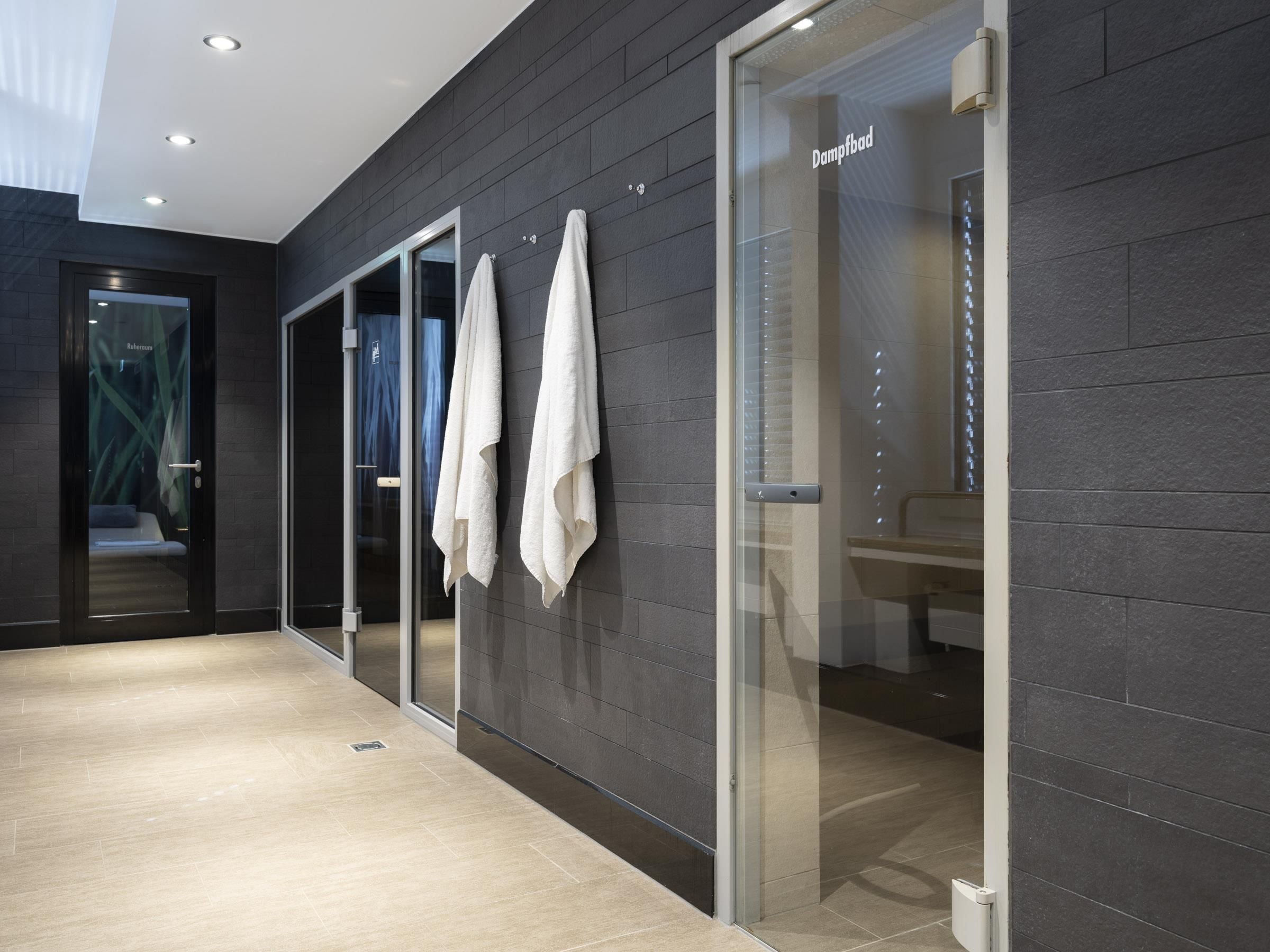 Une salle de bain moderne avec des murs recouverts de carreaux foncés, une douche en verre et un porte-serviettes apparent.
