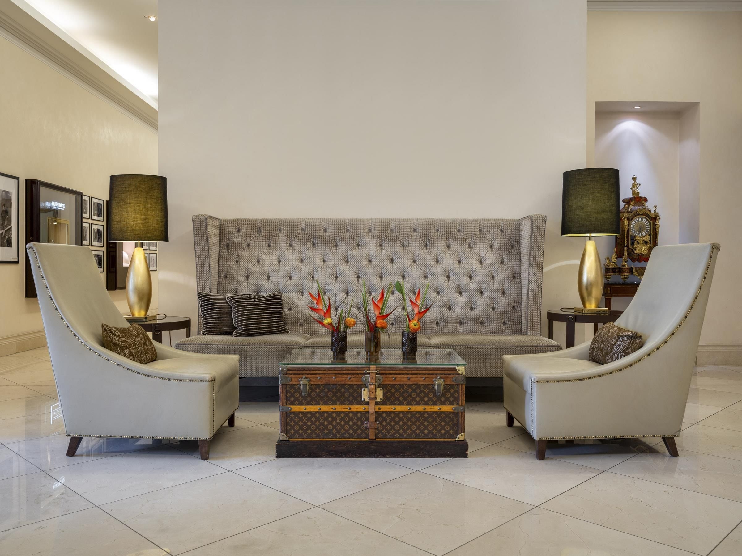 A modern living room with a tufted sofa, two armchairs, a glass coffee table, and decorative vases.