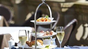 Mesa de comedor al aire libre con tres niveles, platos de comida, copas de vino blanco y una fuente de agua.