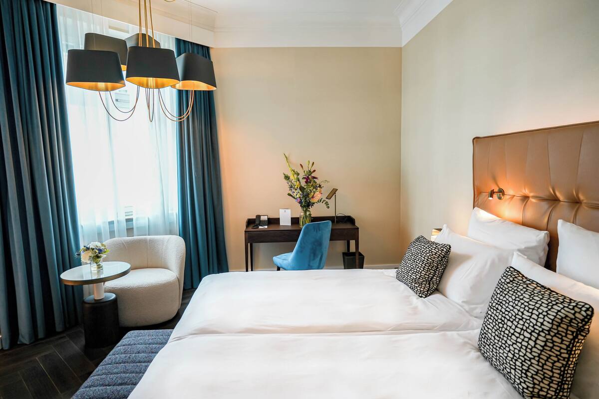 Une chambre d’hôtel avec un grand lit, un bureau avec une chaise, une petite table avec un vase et une lampe.