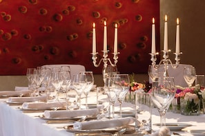 Una mesa dispuesta para una cena formal, con mantelería blanca, cubiertos y cristalería transparente.