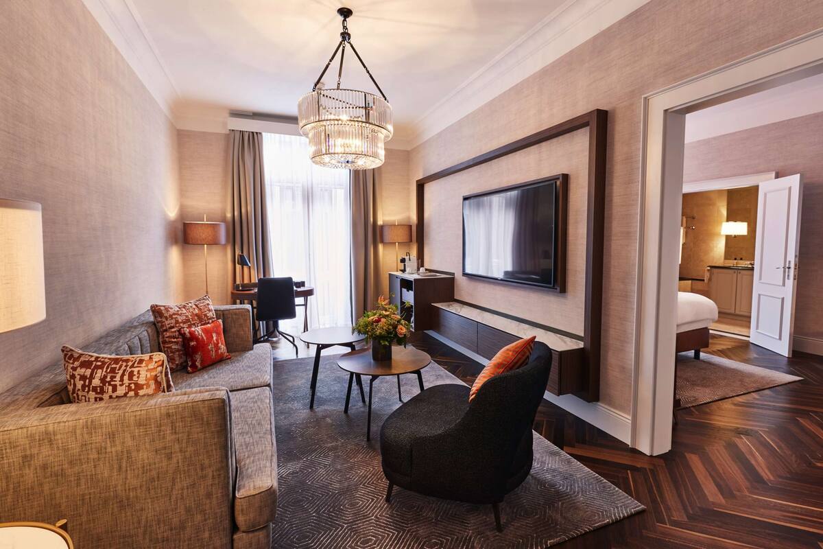 Une chambre d’hôtel moderne équipée d’un canapé, d’un fauteuil, d’une table à manger et d’un téléviseur fixé au mur.