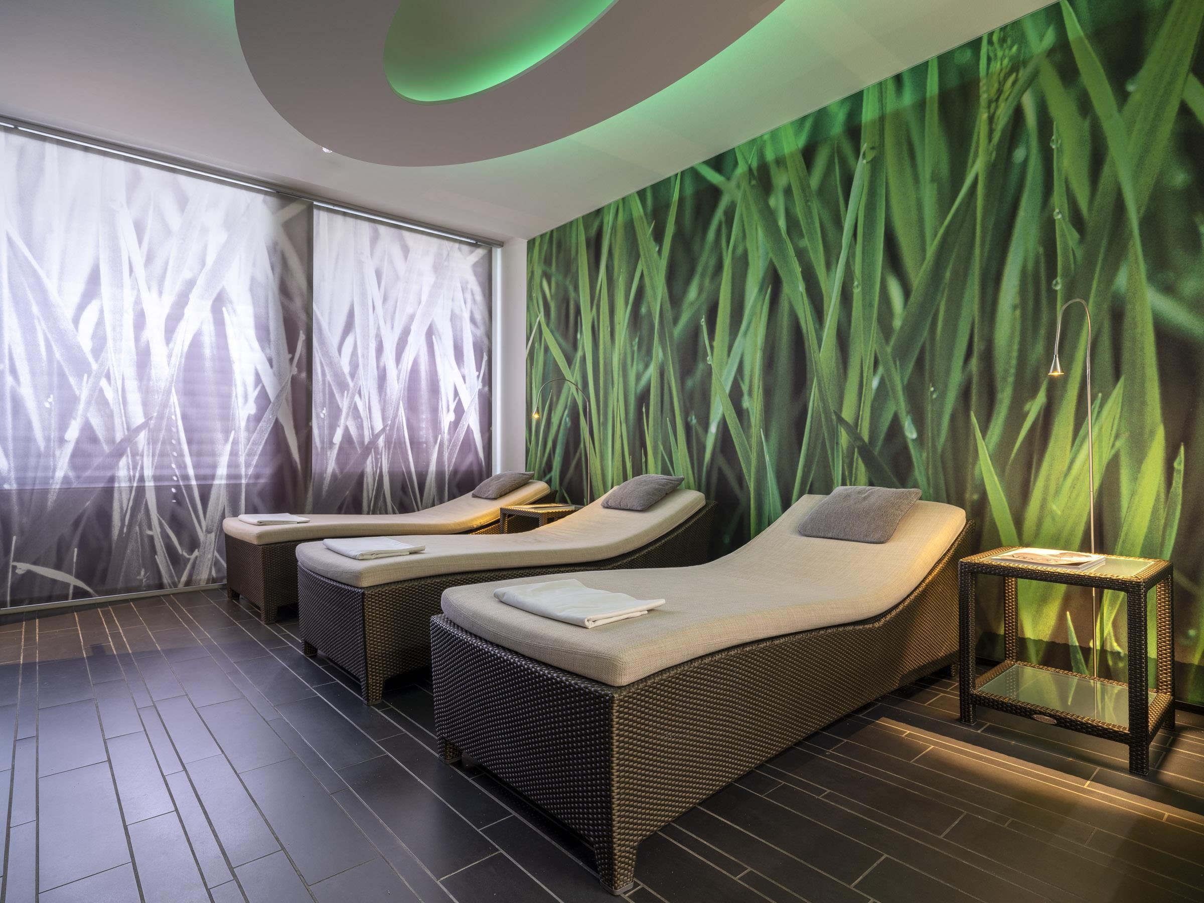 Un cuarto de spa con dos sillones reclinables, una mesita y una pared con un diseño de hojas verdes.