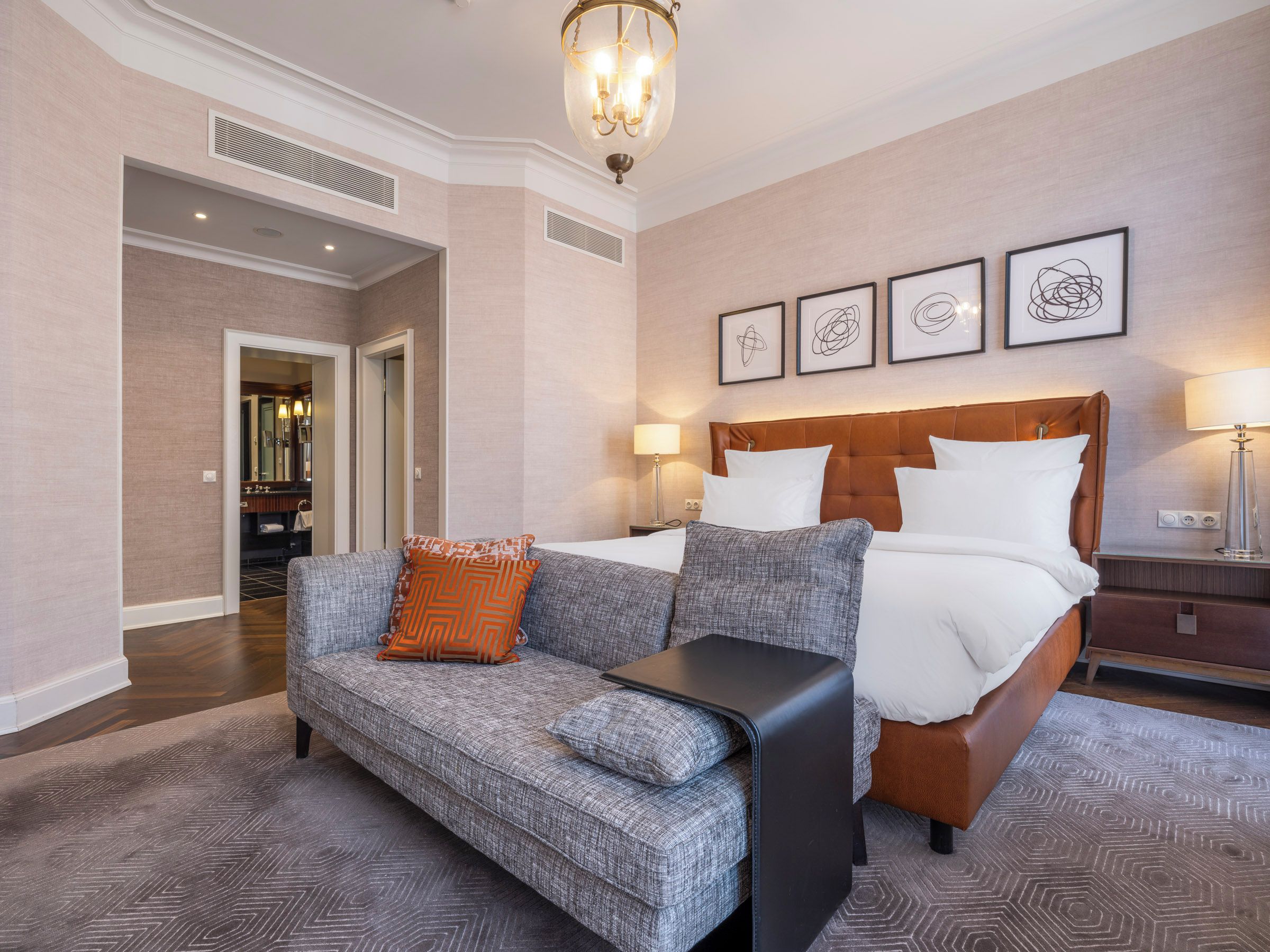 A hotel room with a bed, a sofa, a nightstand, and a chandelier.