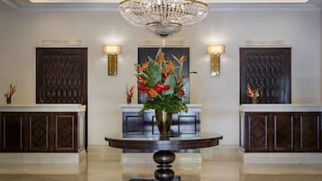 A reception area with a chandelier, two reception desks, and a round table with a vase of flowers.