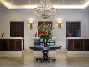 Uma área de recepção com um candelabro, dois balcões de atendimento e uma mesa redonda com um vaso de flores.