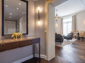 Un interior moderno con un escritorio de madera, un espejo grande y una estatua dorada de rinoceronte. Hay un comedor con una araña y una mesa con sillas.