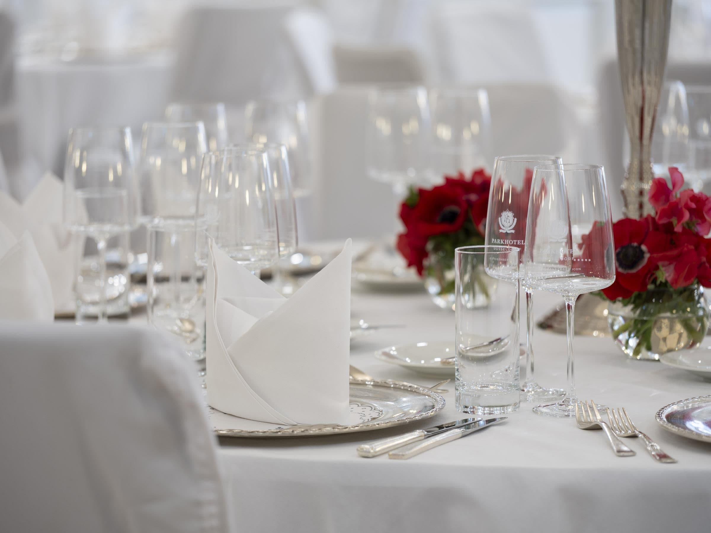 Ein Tisch ist für ein formelles Dinner gedeckt, mit klarem Glas, Besteck und einer weißen Tischdecke.