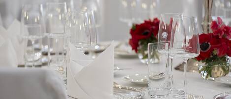 Mesa dispuesta para un evento gastronómico formal, con cristalería transparente, cubiertos y mantel blanco.