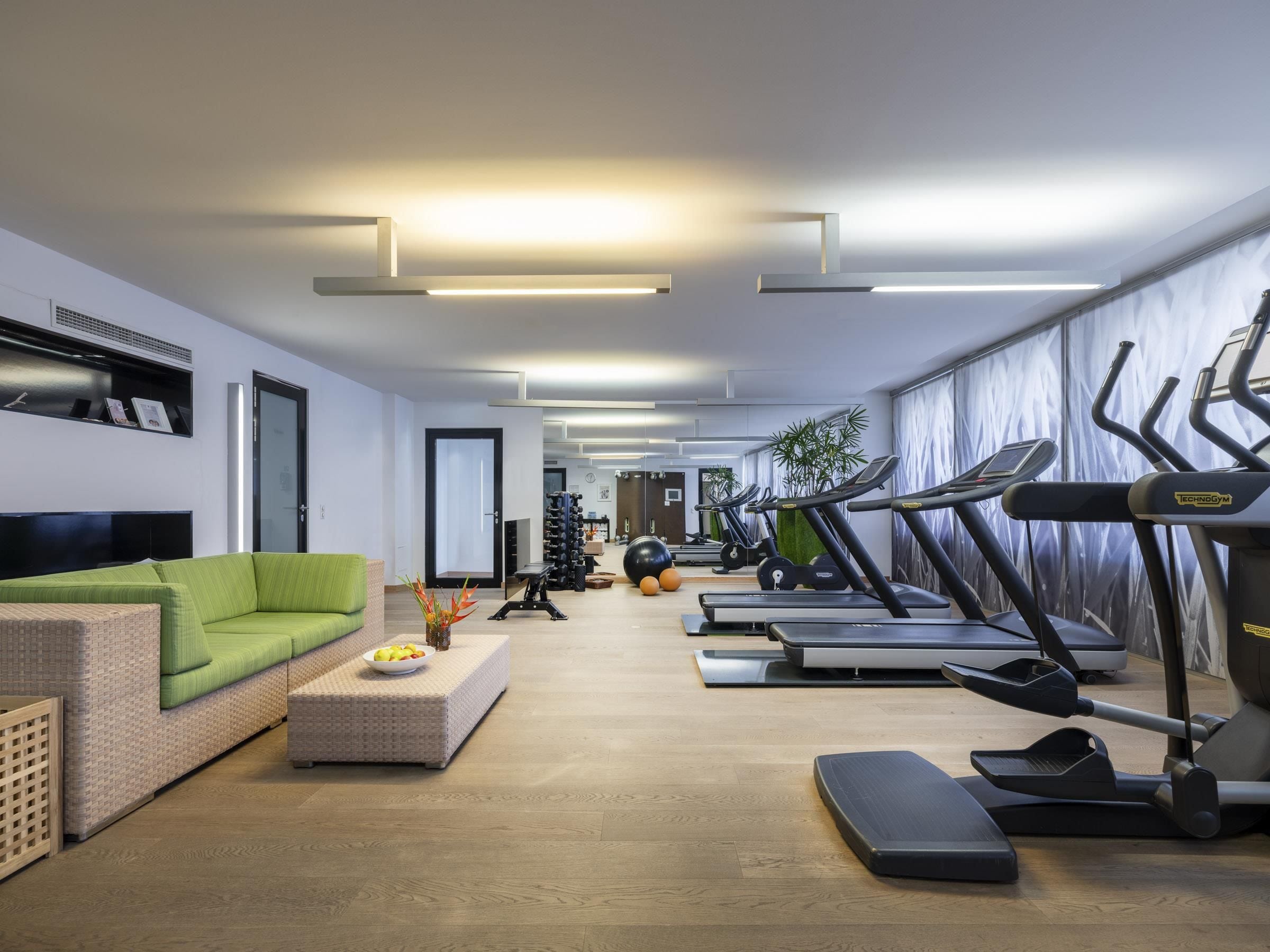 Ein modernes Heimfitnessstudio mit Trainingsgeräten, einem grünen Sofa und einem Holzboden.