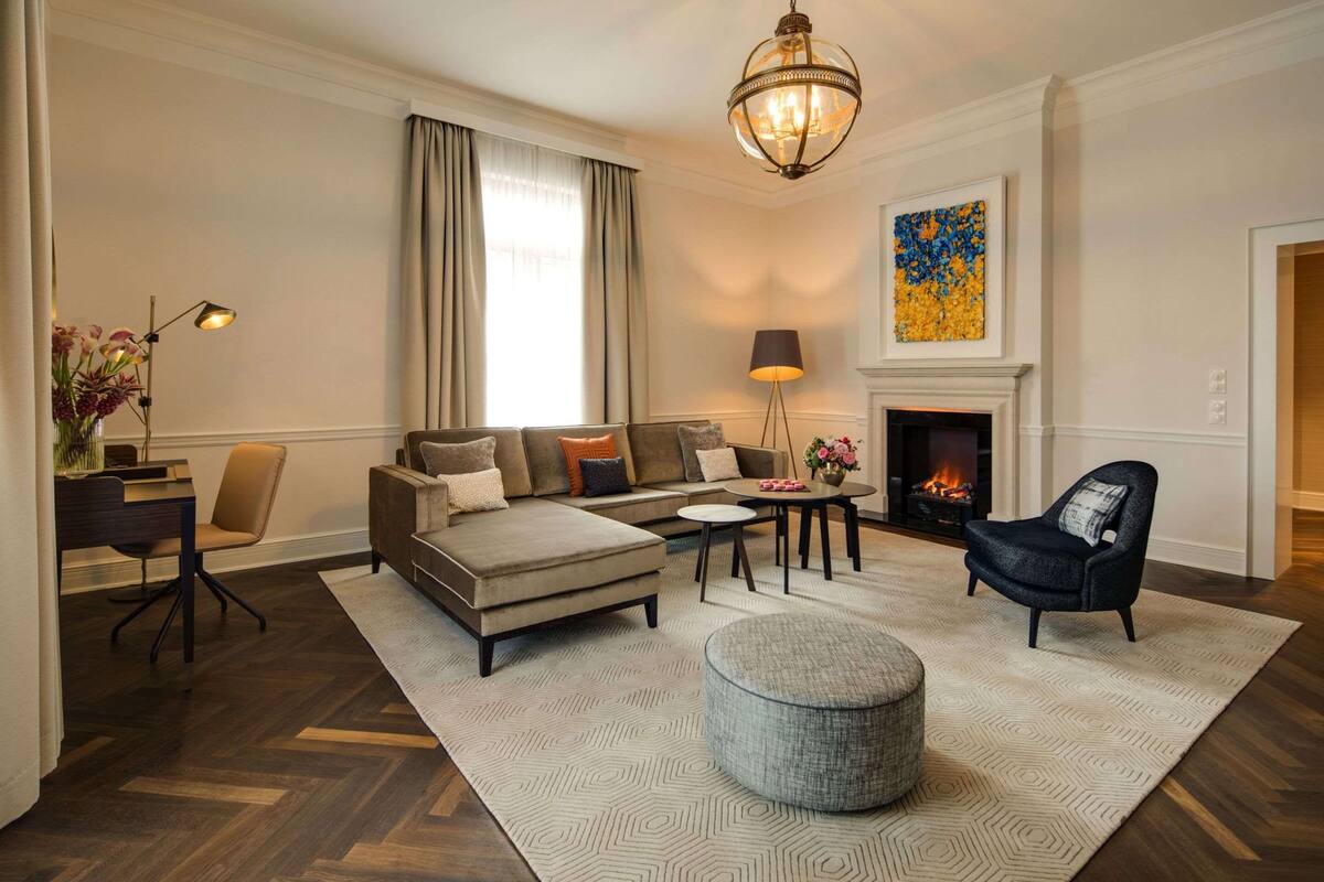 Un salon moderne avec un canapé, un pouf et une table basse, une cheminée et un lustre.