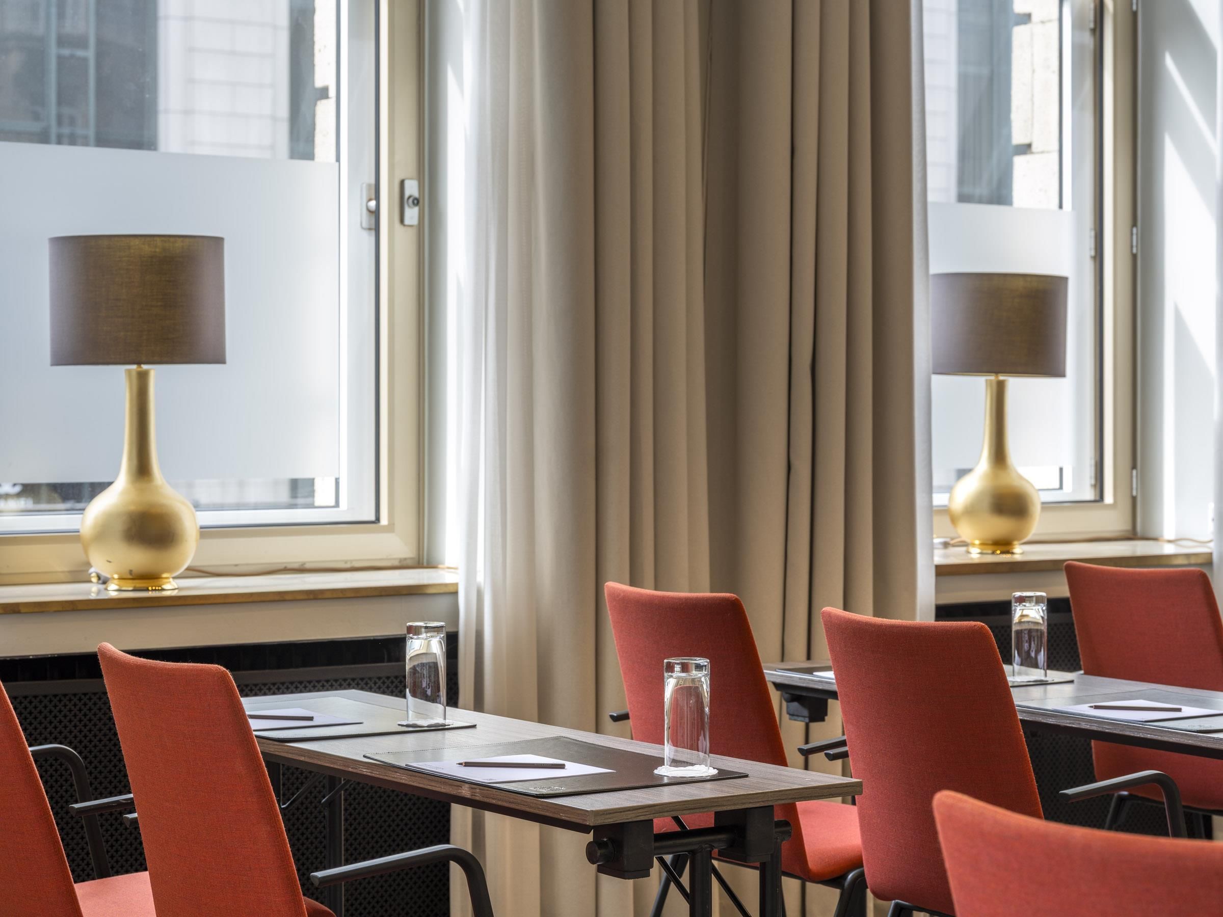 Ett hotellrum med en matplats som har röda stolar, ett träbord och två lampor på fönsterbrädan.