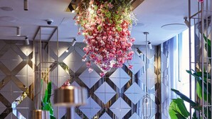 Een moderne lobby met een spiegelende vloer, geometrische muurpatronen en hangende bloemarrangementen.