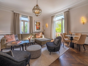 A modern living room with a sofa, ottoman, armchair, and a dining area with chairs and a table.