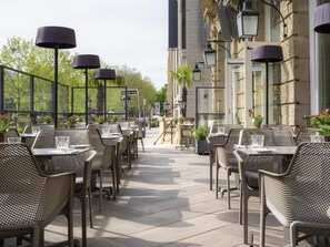 Un espacio de comedor al aire libre con mesas y sillas, farolas y un edificio al fondo.