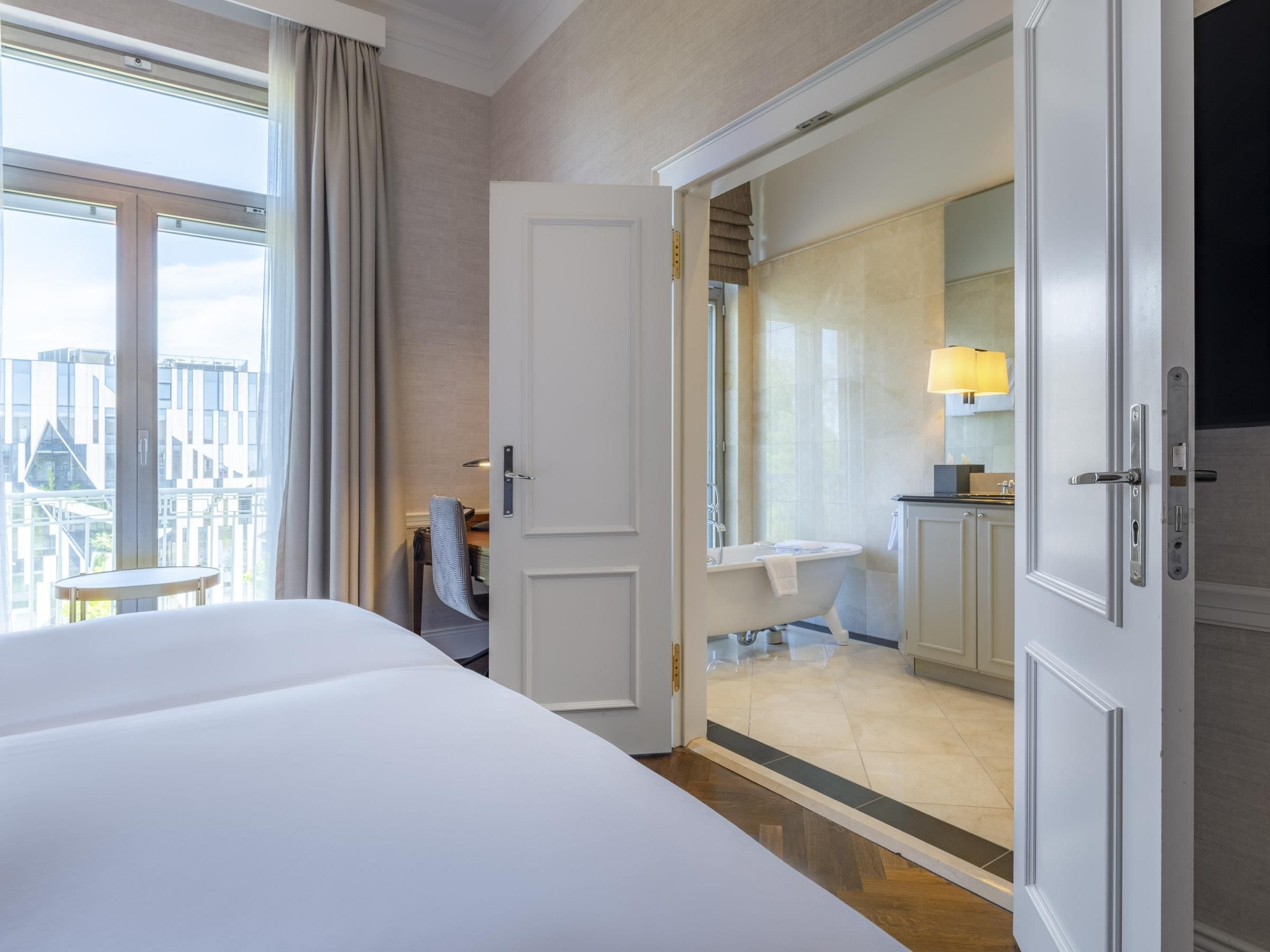 Ein Hotelzimmer mit Bett, Schreibtisch, Stuhl, einem Badezimmer mit Badewanne und Blick auf die Stadt.