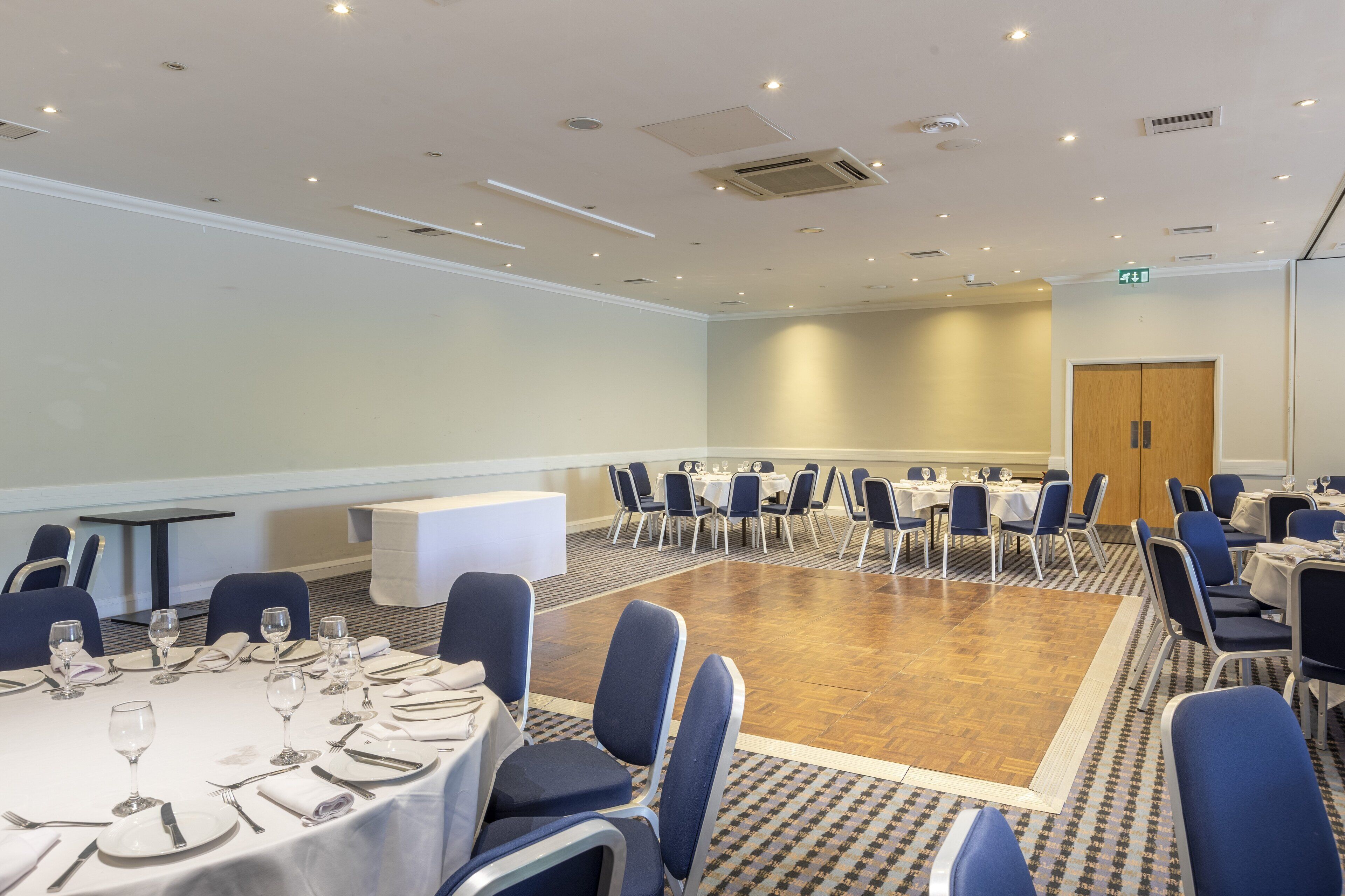 Une salle de conférence avec des tables et des chaises rondes, un plancher en bois et un plafond blanc doté d’un éclairage encastré.