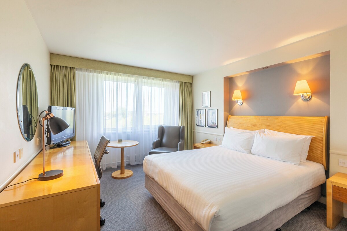 Hotelkamer met een groot bed, een bureau met lamp, een stoel, een klein tafeltje en twee wandlampen.