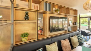 Una sala moderna con un sofá de cuero negro, estanterías de madera con diversos objetos y un televisor de pantalla plana grande.