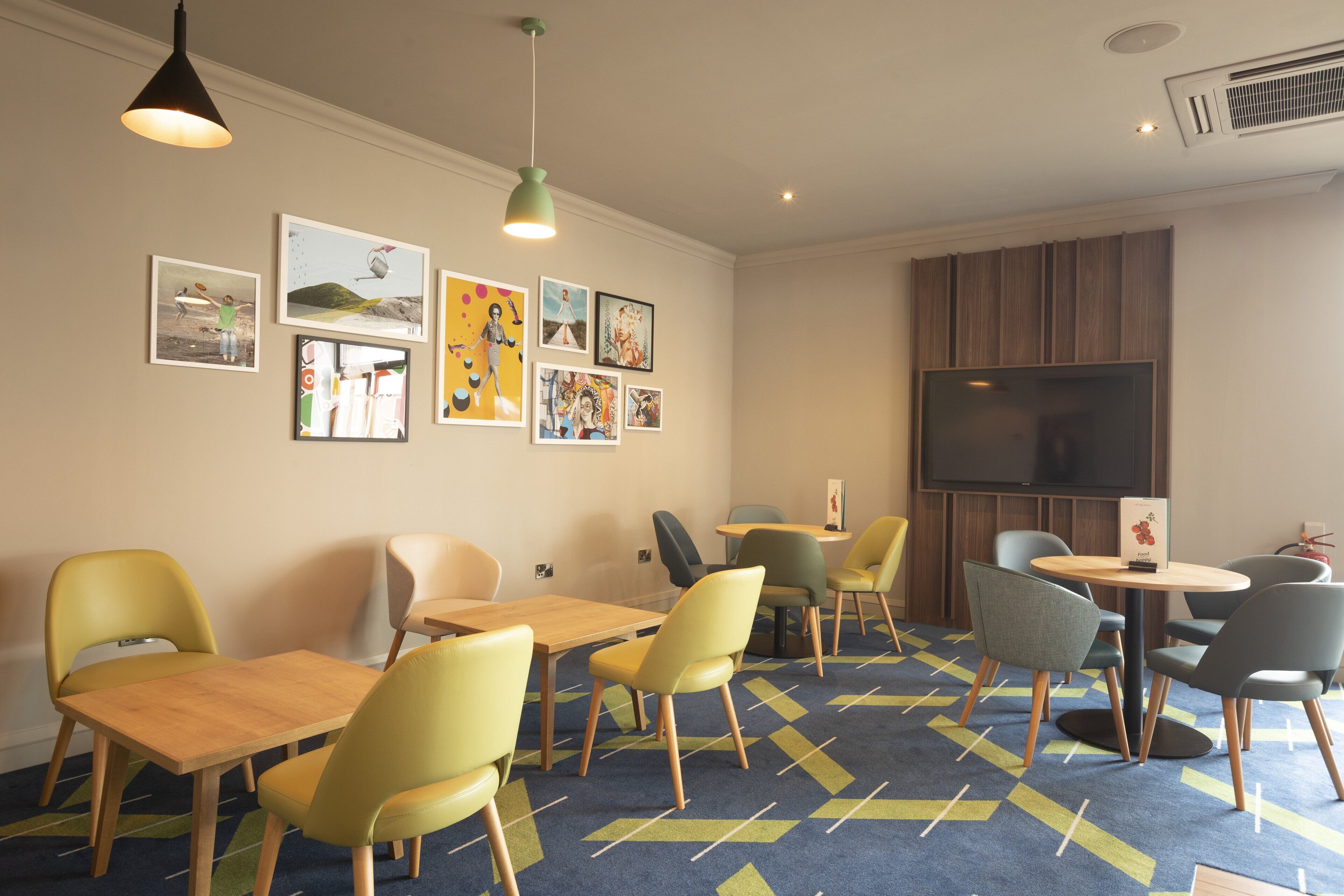 A room with a large TV, multiple tables and chairs, and artwork on the walls.
