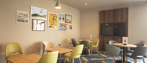 A room with a large TV, multiple tables and chairs, and artwork on the walls.