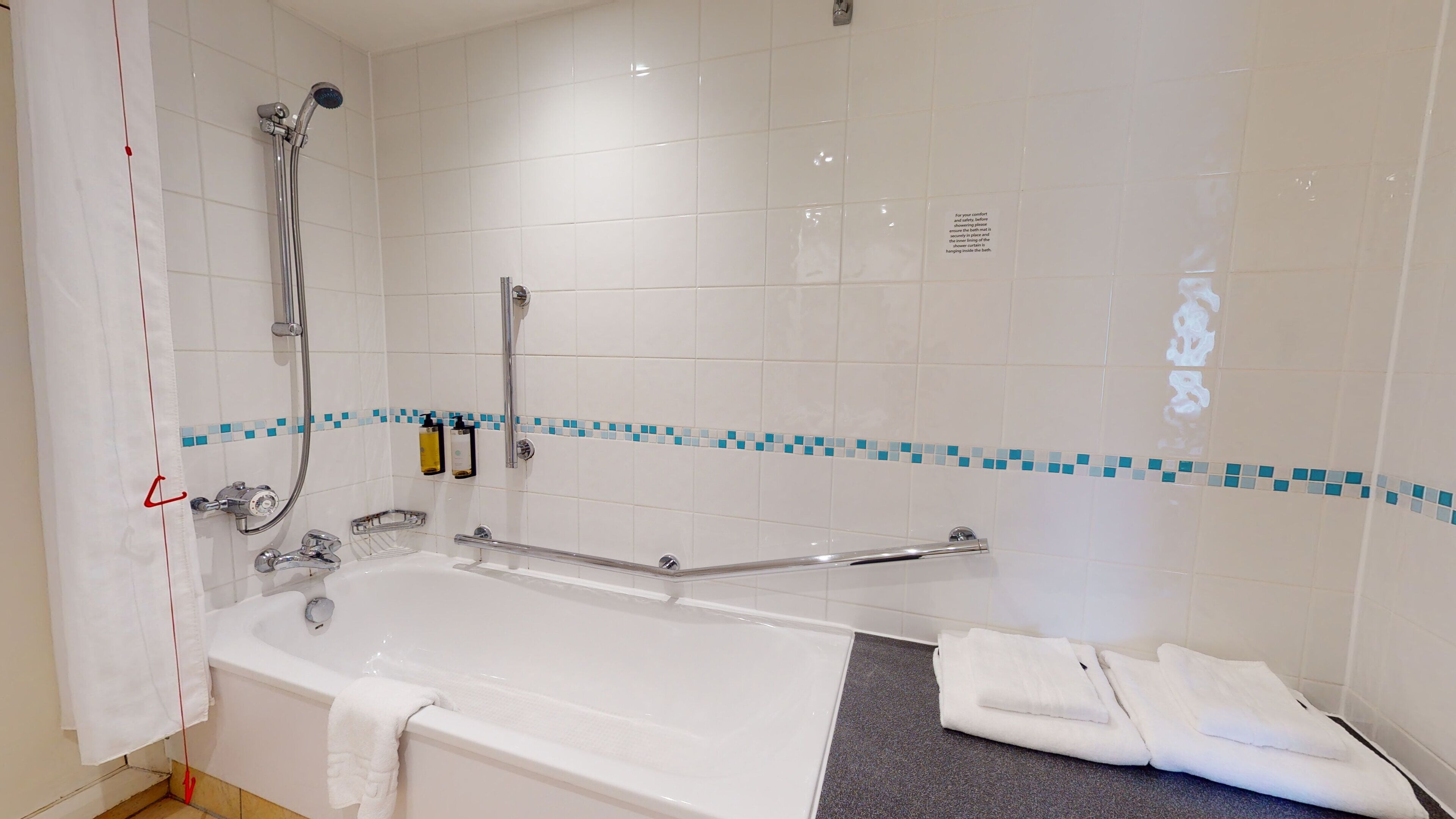 A modern bathroom with a bathtub, shower, and handrails.