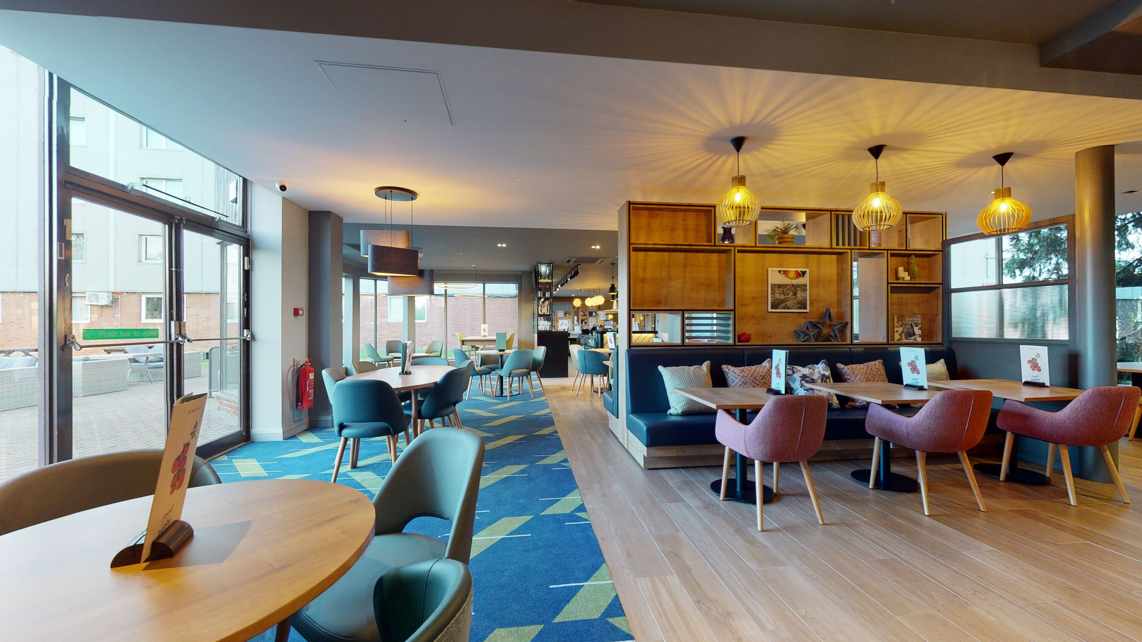 A modern cafe with a mix of seating options including tables and sofas, large windows providing natural light, and a variety of decorative elements on the walls.