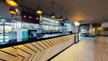 Zona de bar con mostrador de madera, estantes con botellas e iluminación colgante.
